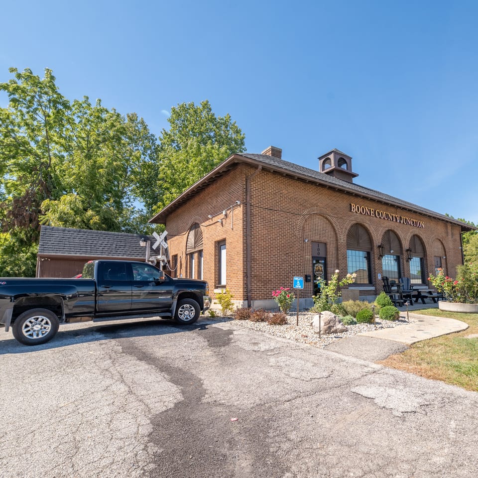 Brick restaurant building labeled Boone County Junction with arched windows, outdoor seating, landscaping, and a parked pickup truck.